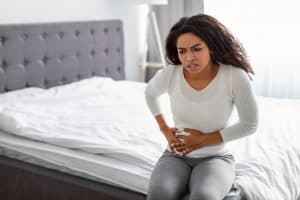Woman sitting on bed and clutching side in pain