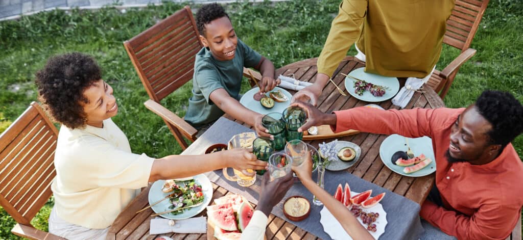 High angle view at group of smiling African American people clinking glasses over table with delicious food outdoors
