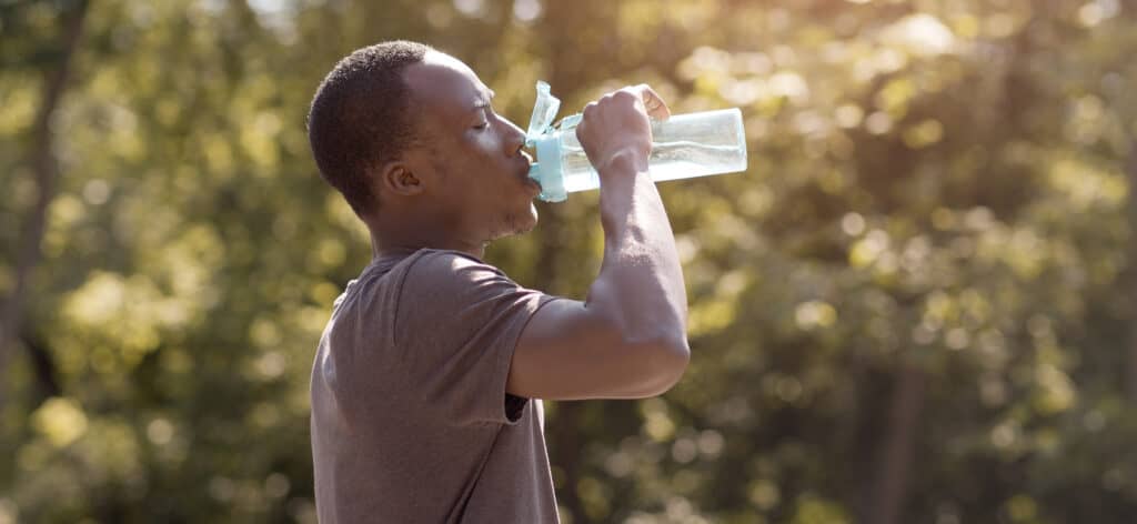 black man drinking water bottle outside